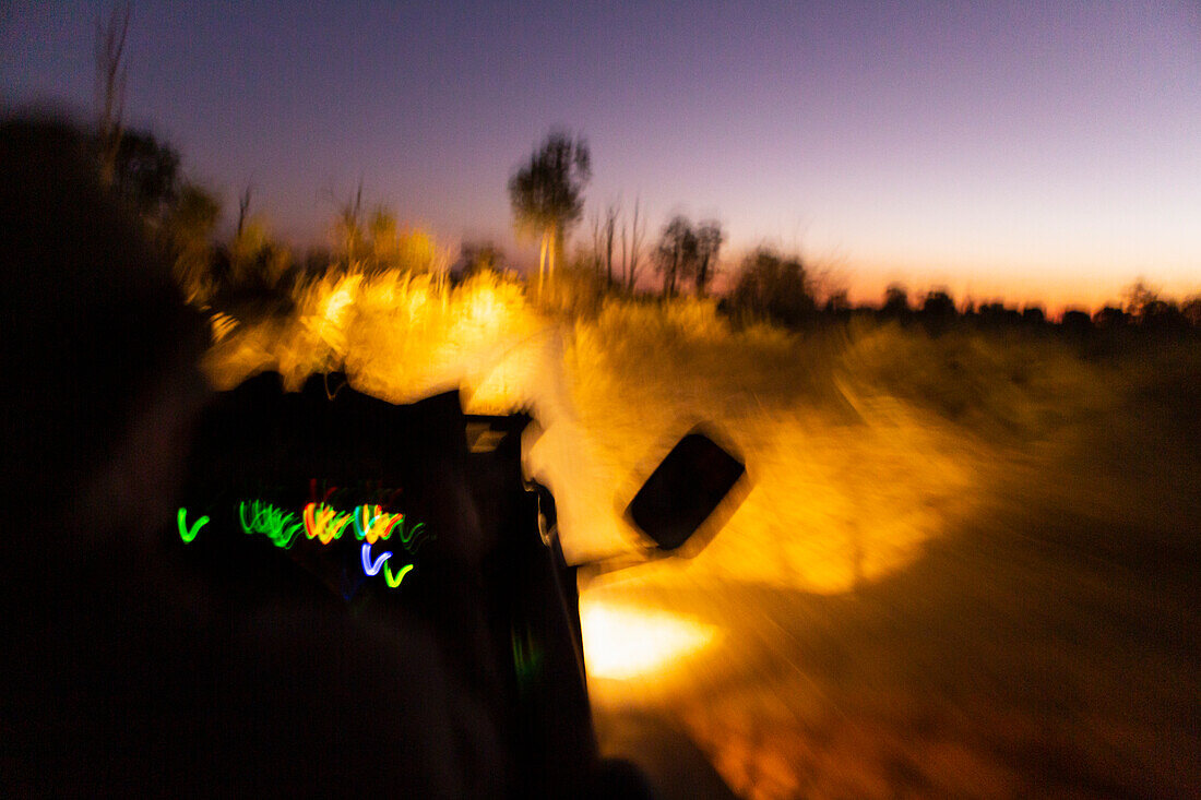 Vehicle with lights moving along a road after sunset.