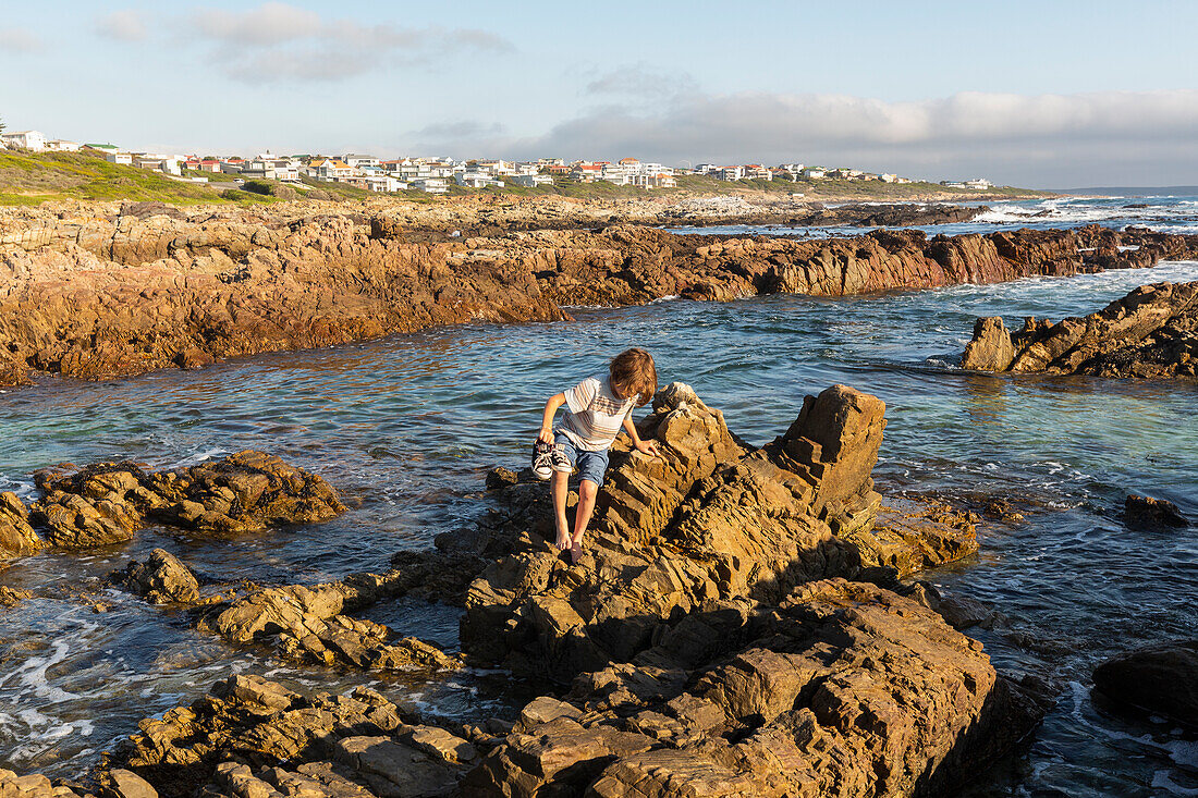 Ein kleiner Junge, der die Felsenbecken an einer zerklüfteten felsigen Atlantikküste, De Kelders, Westkap, Südafrika, erkundet.