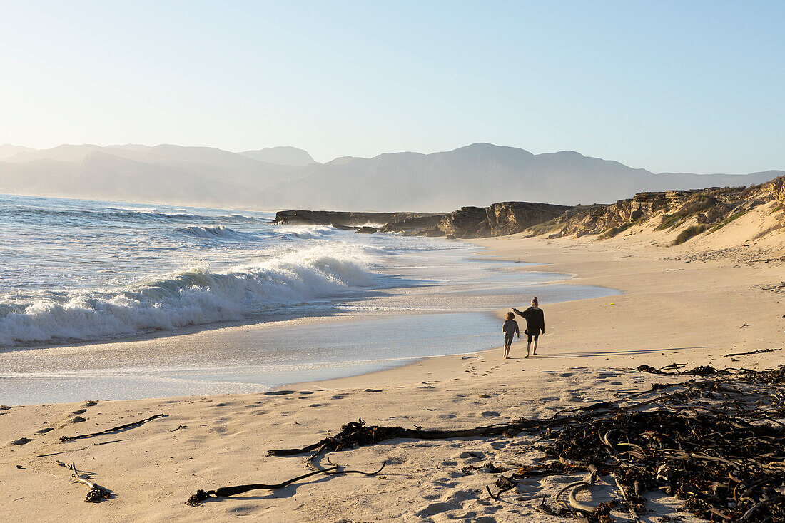 Zwei Menschen, die an einem Sandstrand spazieren, ein Teenager und ein Junge