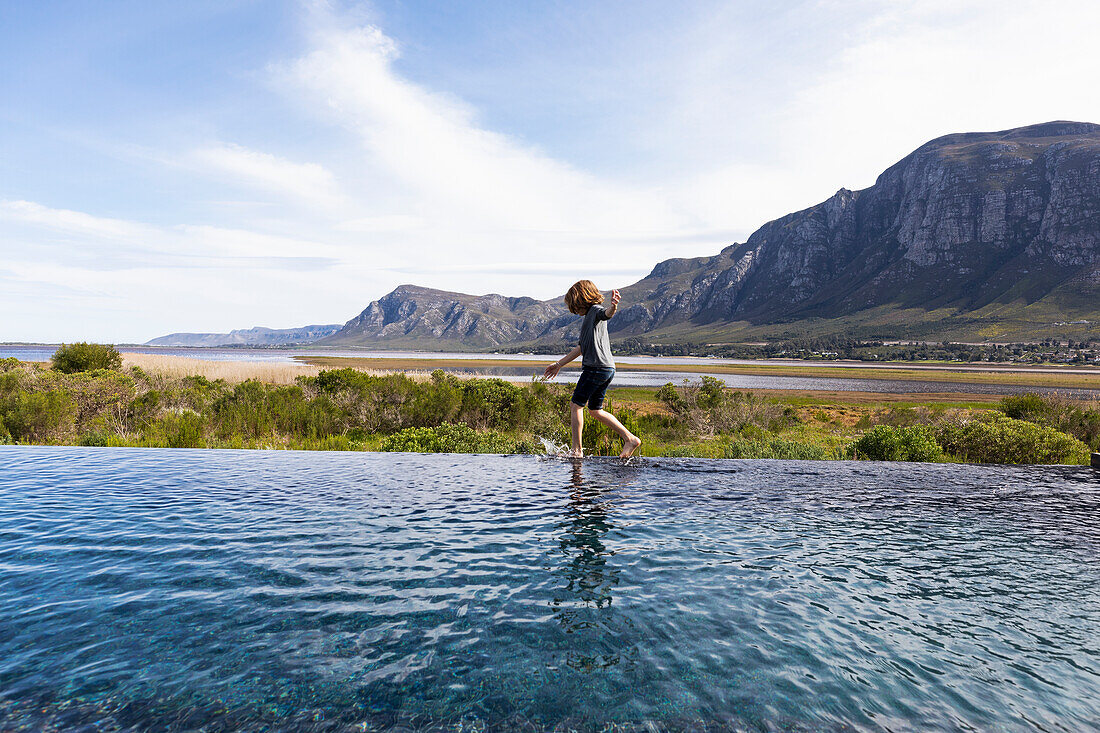 Eight year old boy walking around the edge of an infinity pool, a mountain backdrop, Klein Mountains, South Africa
