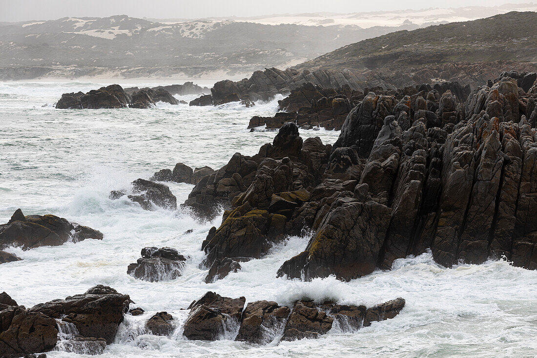 Schroffe Felsen und die felsige Küste des Atlantiks am Strand von De Kelders, Wellen, die sich am Ufer brechen, Südafrika