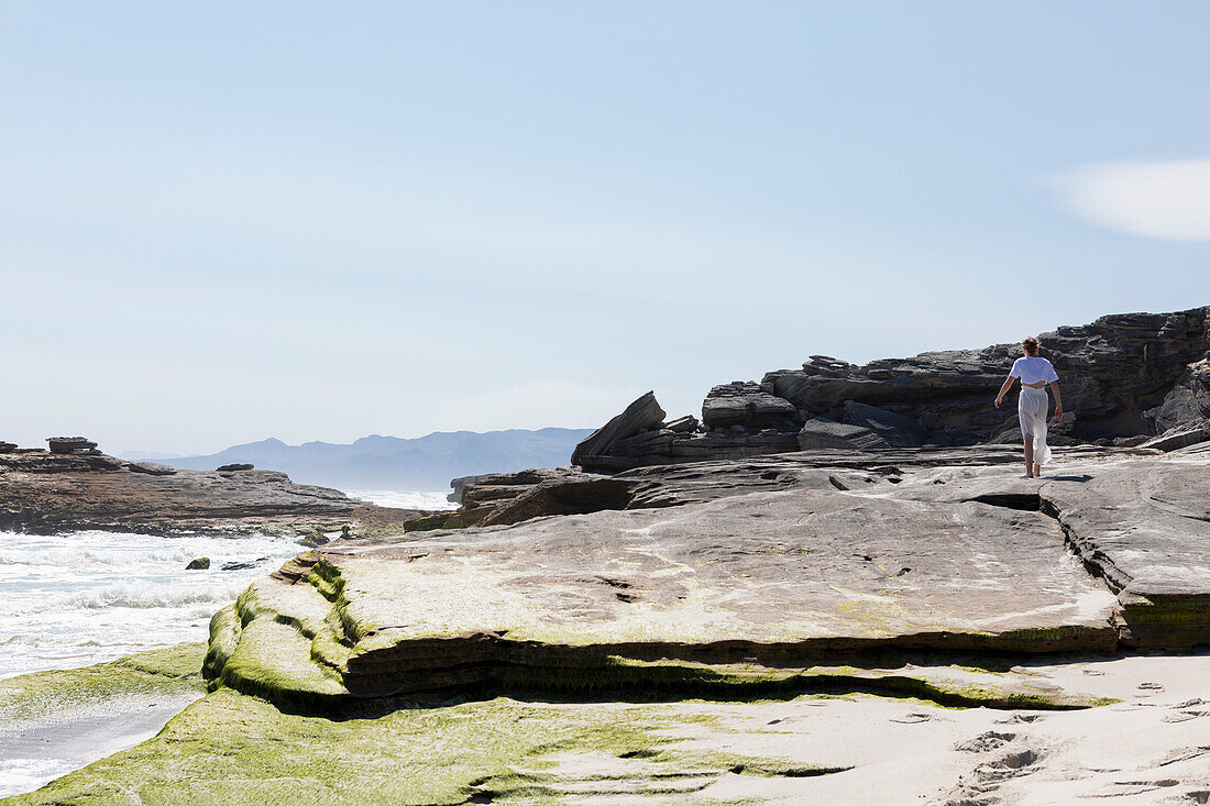 Teenage girl exploring a rocky shore on the Atlantic ocean coastline, South Africa