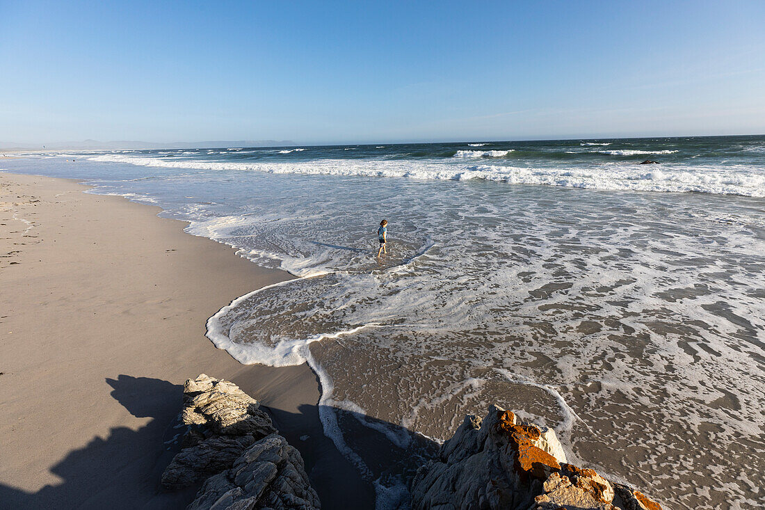 Boy playing in in surf at the water's edge on a wide sandy beach, Grotto Beach, South Africa