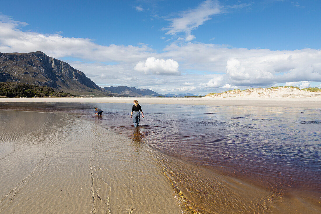 Teenage girl and young boy on an open sandy beach wading through shallow water, Grotto Beach, South Africa