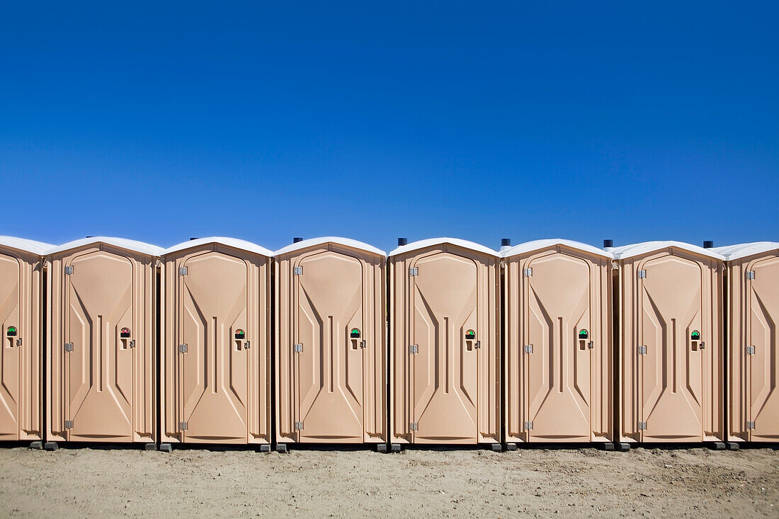 Portable toilets at the beach, in a row.