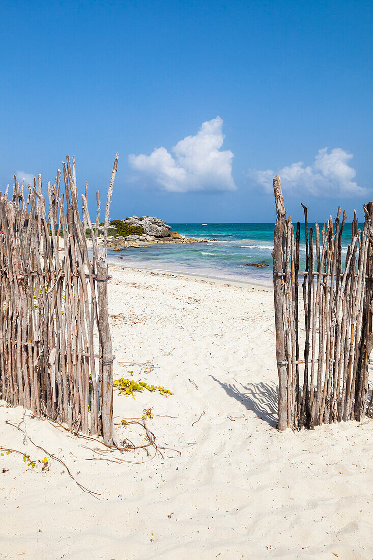 An opening in the fence onto a white sand beach