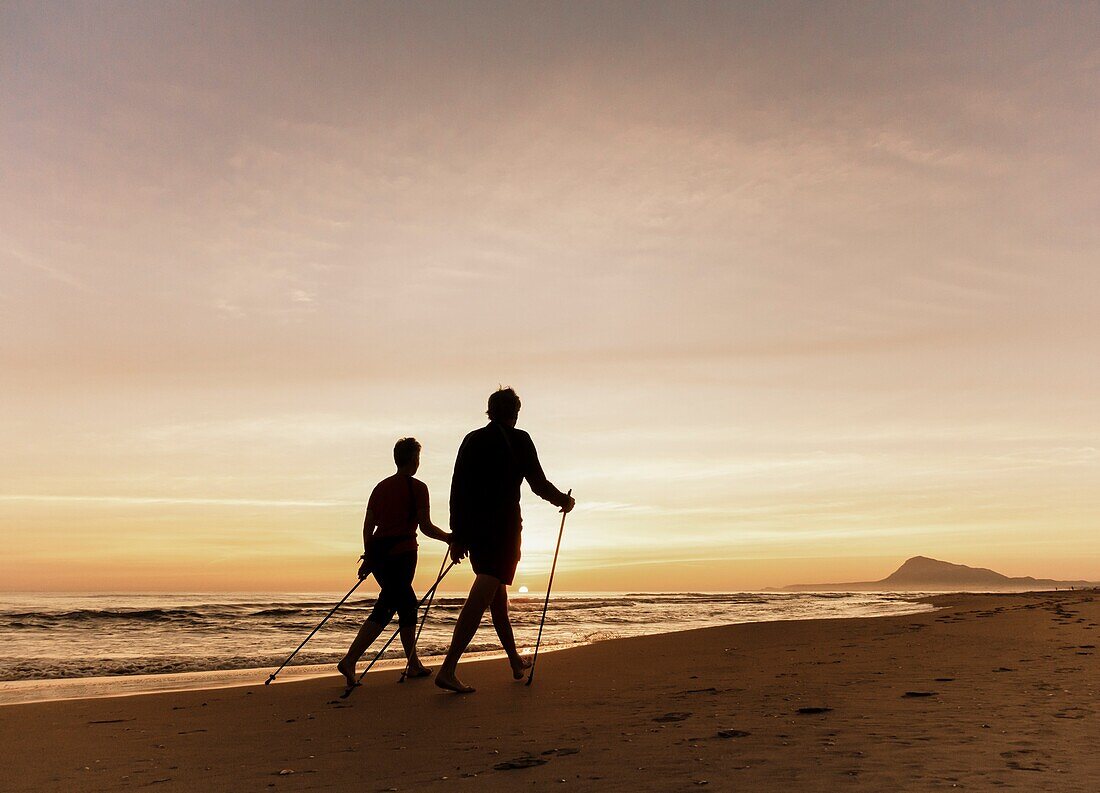 Mature couple walking on beach at sunrise near Oliva on the Costa del Azahar near Denia,Valencia province,Spain,Europe.