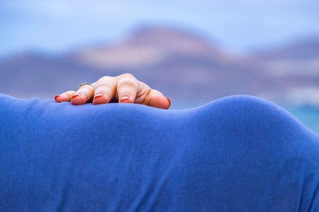 Hand mit Verlobungsring auf einem weiblichen Bauch vor Bergen in Las Palmas de Gran Canaria.
