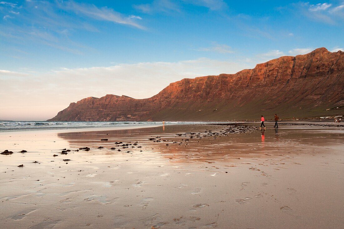 Sonnenuntergang am Ufer eines Strandes mit Personen, die am Ufer des Meeres spazieren gehen. Famara, Lanzarote. Spanien.