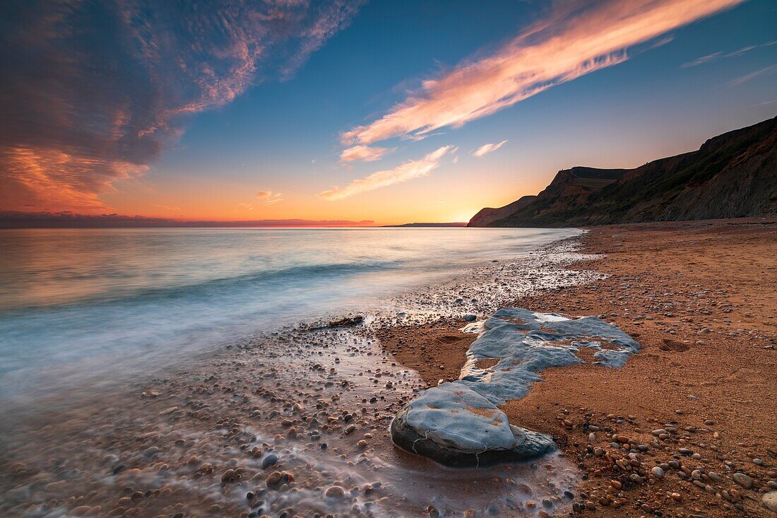 Sonnenuntergang vom Eype Mouth Beach an Dorsets Jurassic Coast World Heritage Site, aufgenommen Mitte September mit Thorncombe Beacon in der Ferne. Eine lange Verschlusszeit wurde verwendet, um die Bewegung des Wassers im Ärmelkanal zu verwischen.