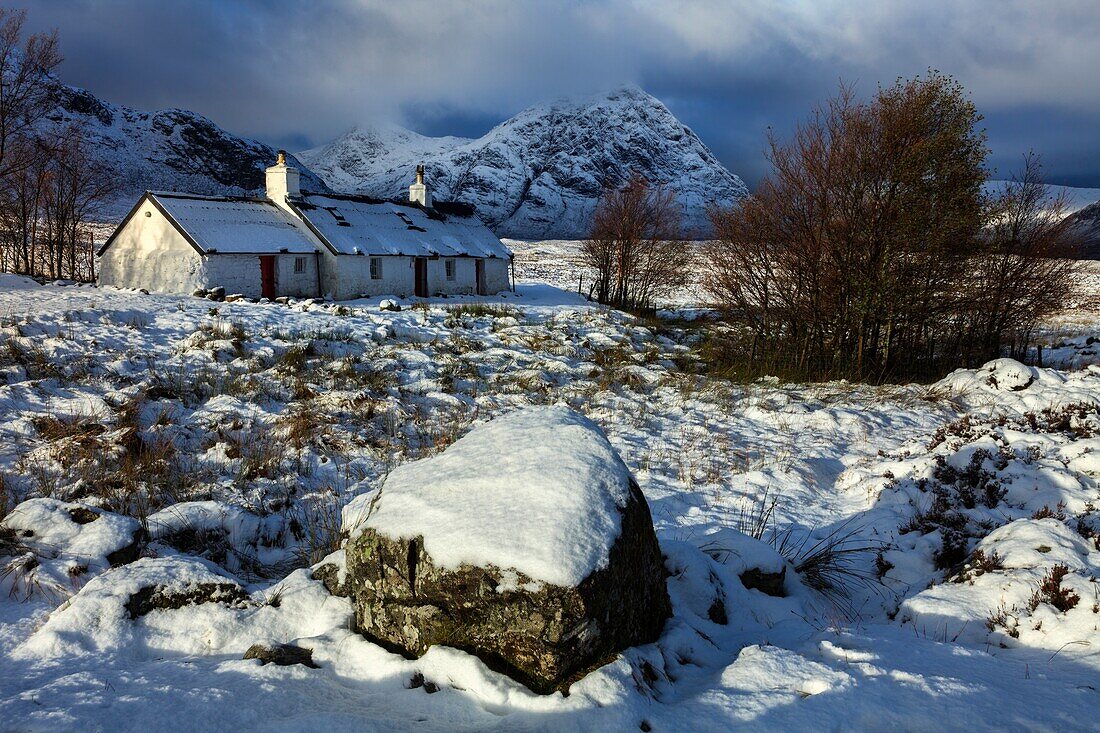 Black Rock Cottage auf Rannoch Moor in den schottischen Highlands, beleuchtet von den ersten Sonnenstrahlen nach einem nächtlichen Schneefall Anfang November.