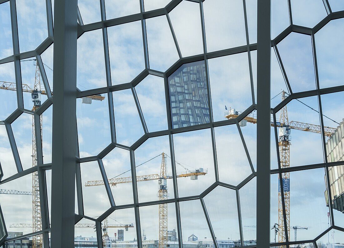 Construction boom,cranes seen through the facade of Harpa,the new concert hall. Reykjavik,the capital of Iceland during winter. Northern Europe,Scandinavia,Iceland,February.