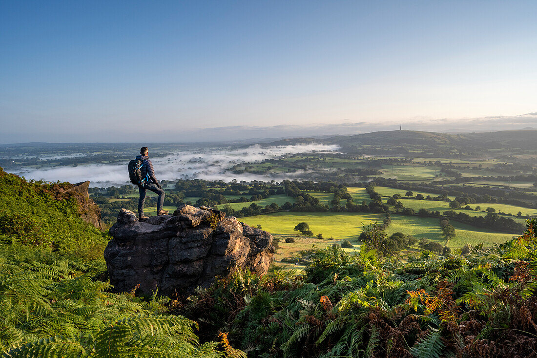Ein Walker stand auf einem Felsen am Cloudside mit Blick über die Cheshire Plains, Congleton, Cheshire, England, Vereinigtes Königreich, Europa
