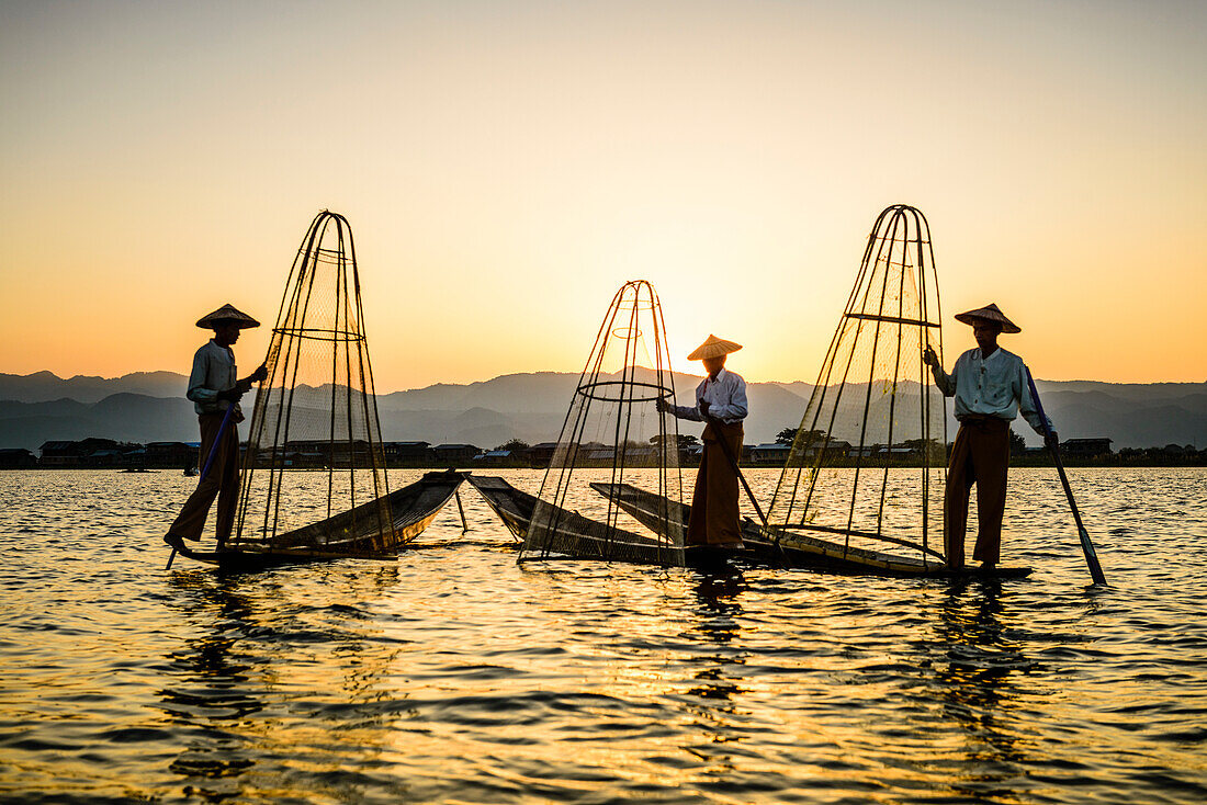 Three fishermen fishing on Lake Inles using traditional cone shape fishing nets.