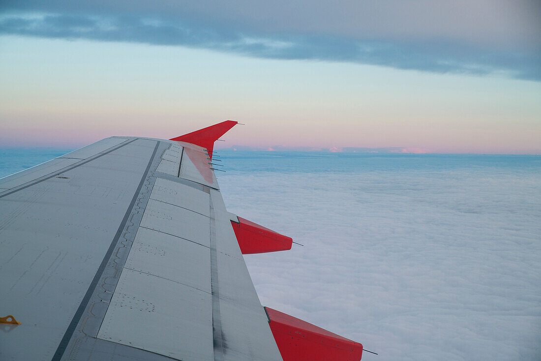 Airplane wing above clouds at sunset