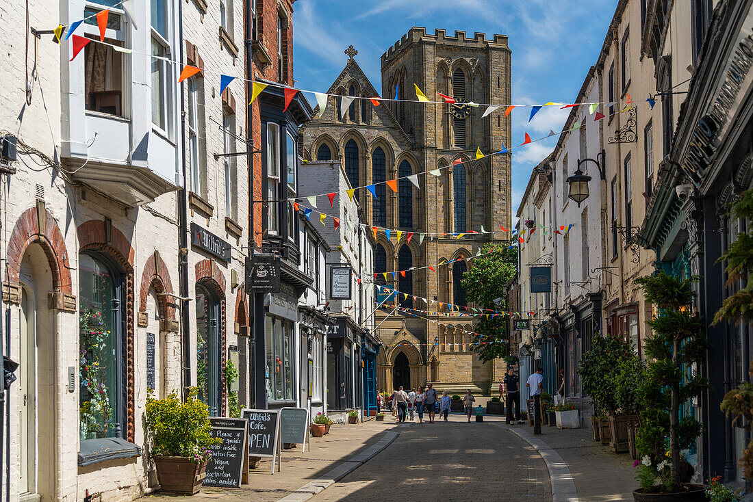 Blick auf Geschäfte und Cafés auf Kirkgate und die Kathedrale im Hintergrund, Ripon, North Yorkshire, England, Vereinigtes Königreich, Europa