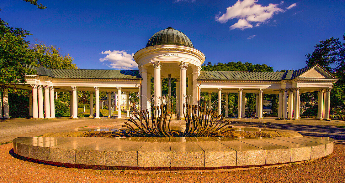 View across a fountain to the Caroline Colonnade built in 1871/72 in Marienbad, Mariánské Lázne, Czech Republic