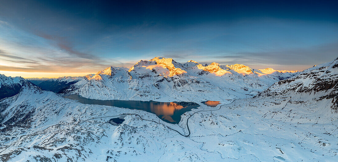 Kurvenreiche Straße des Berninapasses in der Winterlandschaft in der Nähe des zugefrorenen Lago Bianco bei Sonnenaufgang, Engadin, Graubünden, Schweiz, Europa