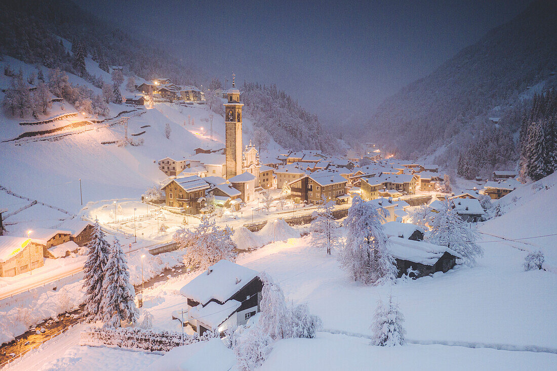 Illuminated village of Gerola Alta and frozen river covered with snow during winter dusk, Valgerola, Valtellina, Lombardy, Italy, Europe