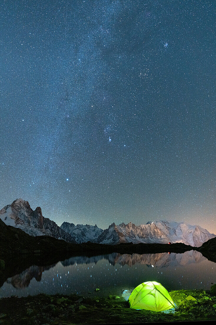 Milky Way glowing over Mont Blanc massif covered with snow and camping tent on shore of Lacs des Cheserys, Haute Savoie, French Alps, France, Europe