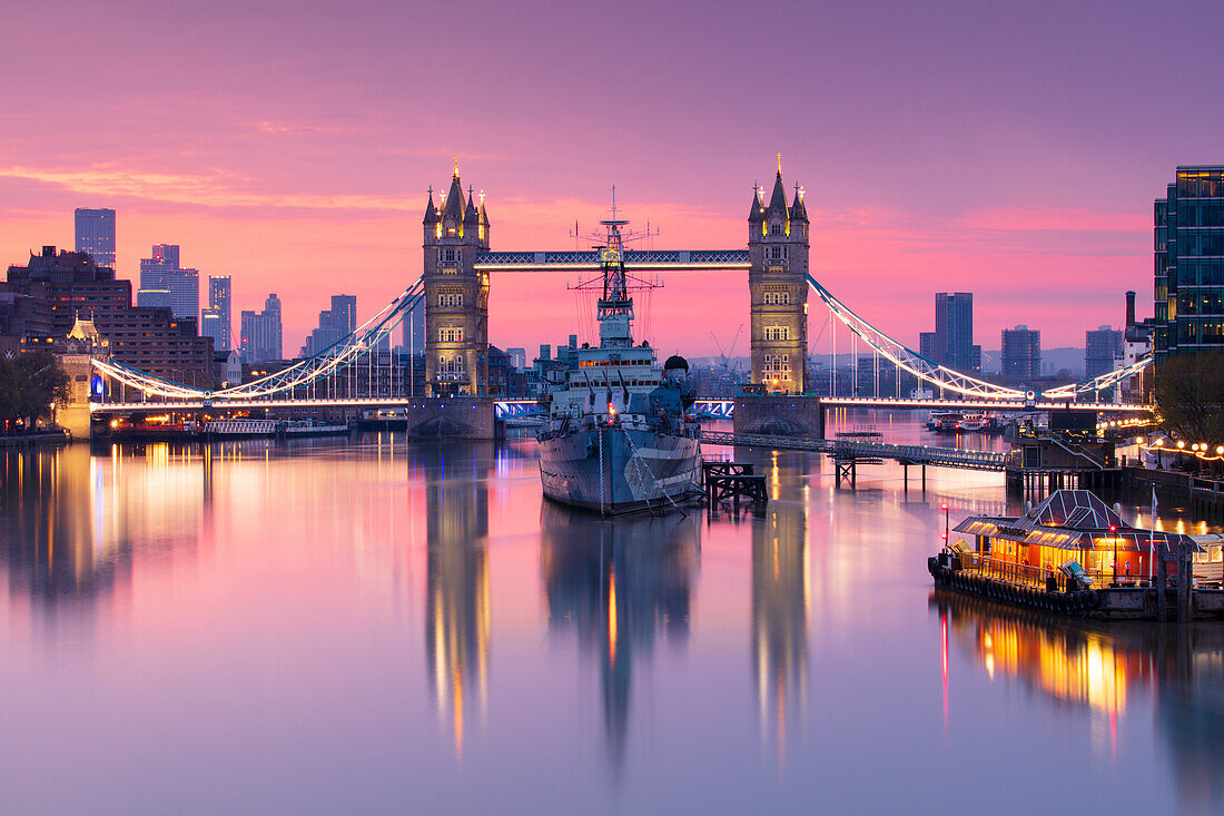 Sonnenaufgangsansicht der HMS Belfast und der Tower Bridge, die sich in der Themse widerspiegeln, mit Canary Wharf im Hintergrund, London, England, Vereinigtes Königreich, Europa