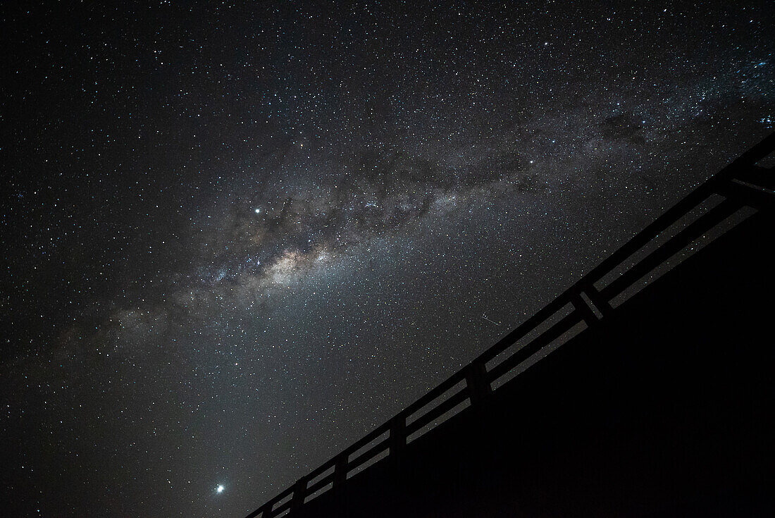 Low angle view of bridge with railing against milky way in sky