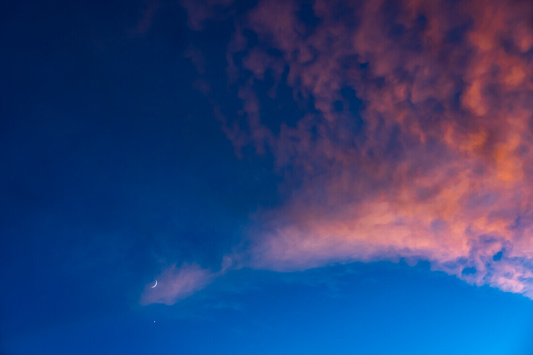 Crescent moon against blue sky with pink clouds