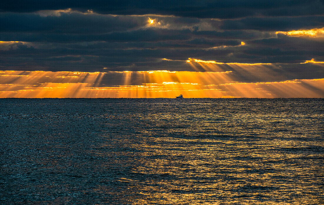 Sunrays and golden clouds over ocean at sunrise with small fishing boat in distance