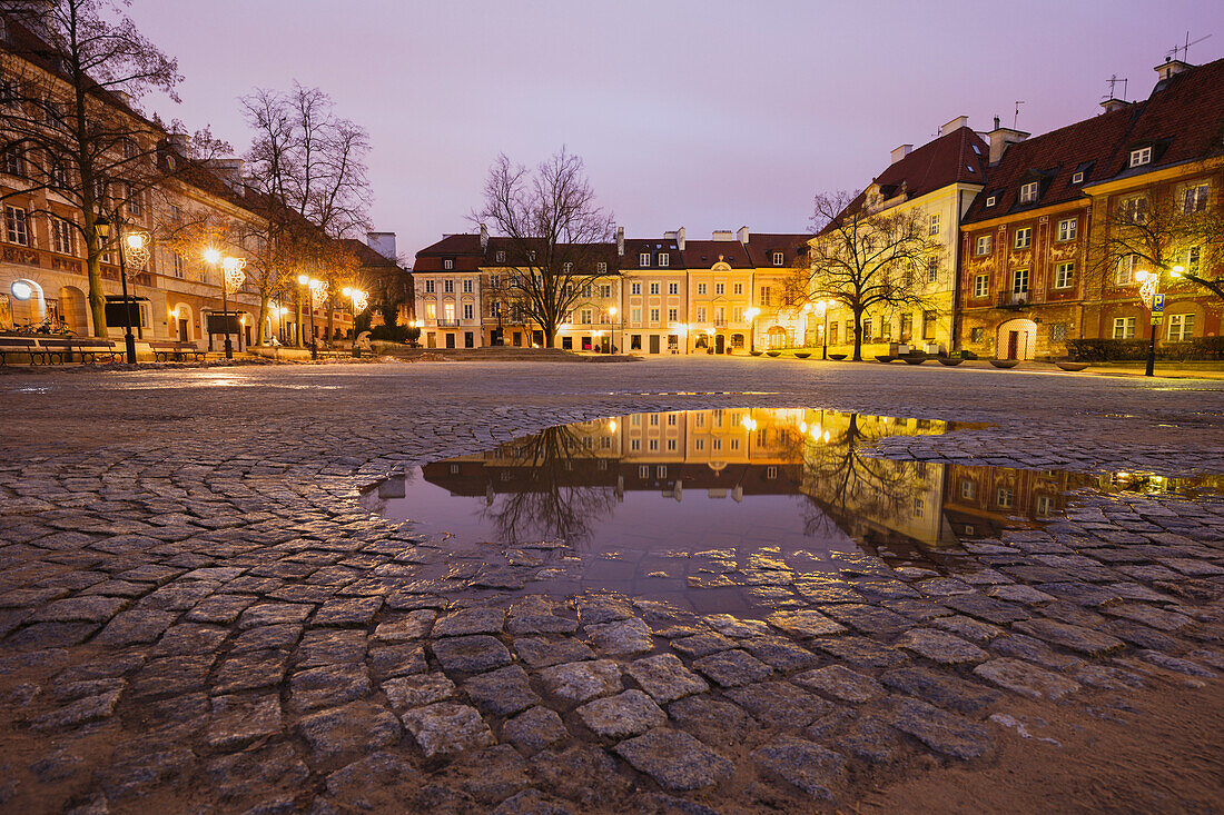 Polen, Masowien, Warschau, beleuchteter Stadtplatz, der nachts in der Pfütze reflektiert wird