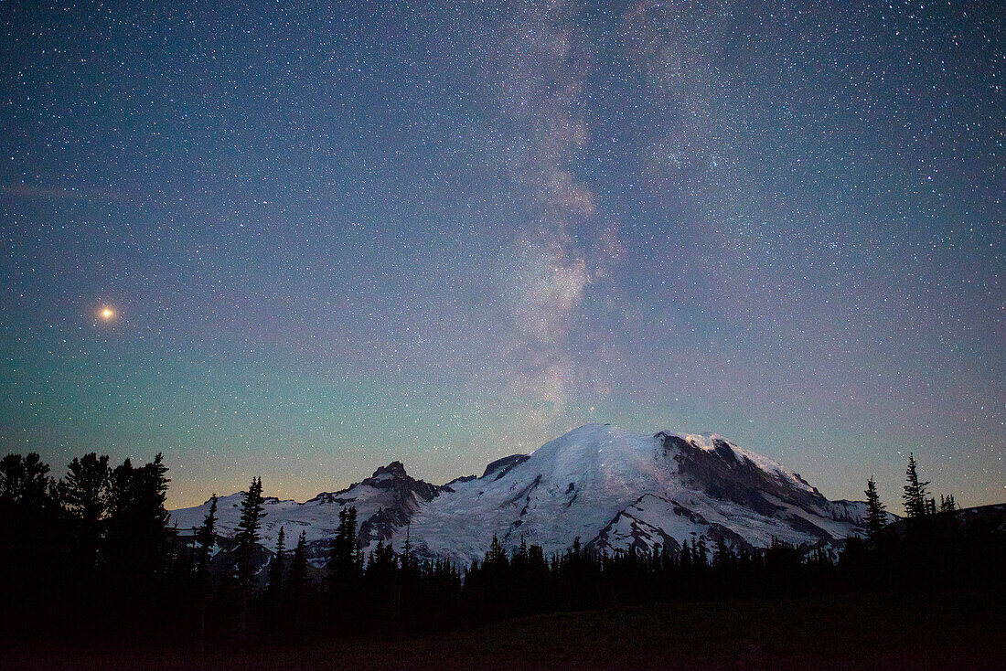 The lights of climbers can be seen on the mountain as the Milky Way rises behind Mt. Rainier National Park, Washington State.