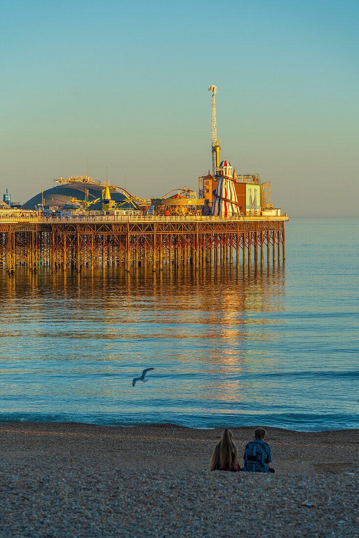 View of couple on beach and Brighton Palace Pier at sunset, Brighton, East Sussex, England, United Kingdom, Europe