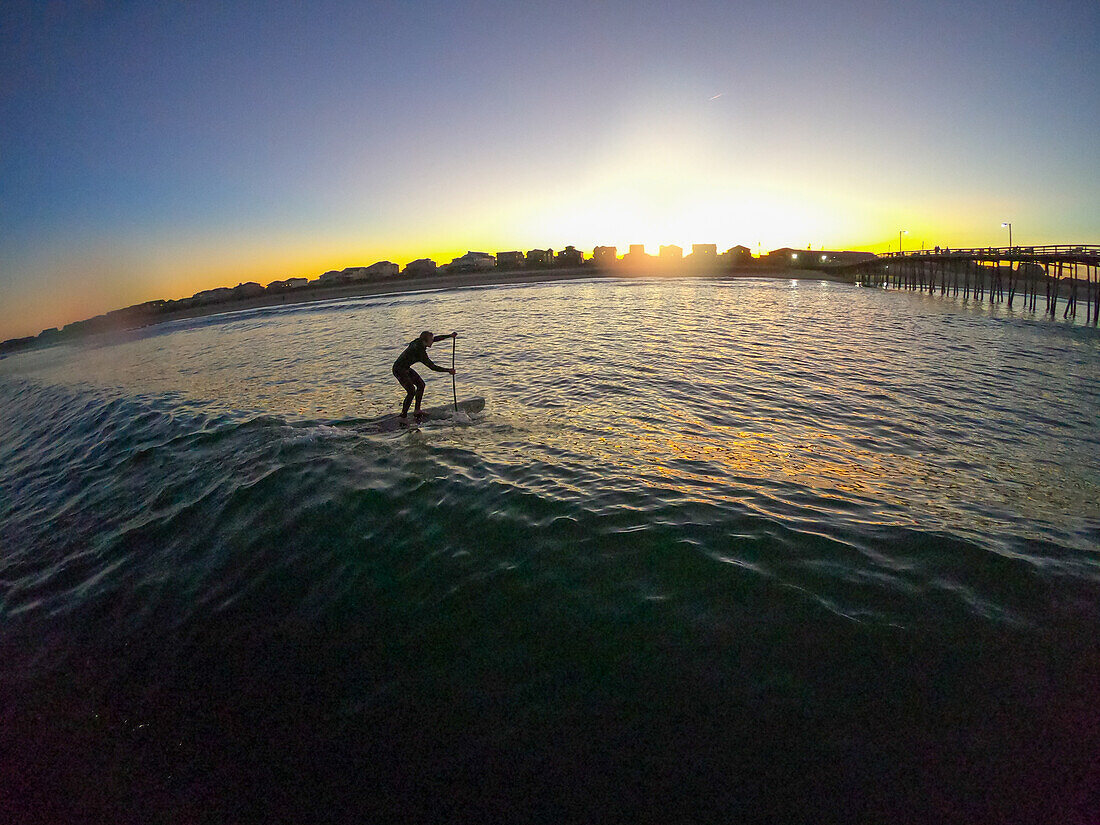 Stand Up Paddle Boarder fängt eine Welle bei Sonnenuntergang, Nags Head, North Carolina, Vereinigte Staaten von Amerika, Nordamerika
