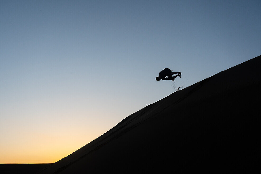 Silhouette eines Mannes, der eine Sanddüne in Nags Head, North Carolina, Vereinigte Staaten von Amerika, Nordamerika hinunterstürzt