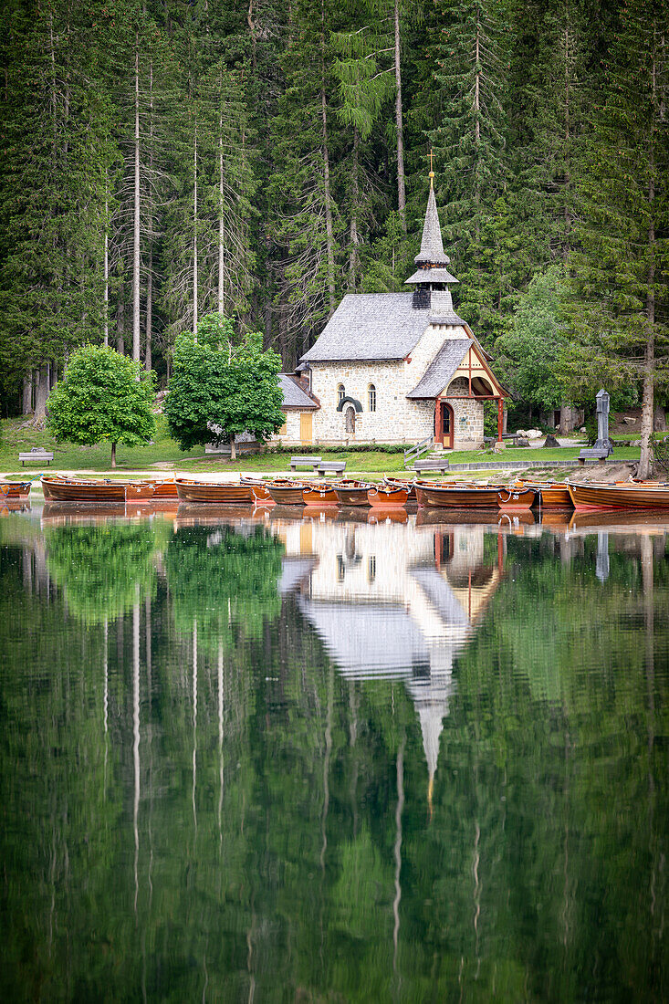 Grüner Wald und Kapelle spiegeln sich im Sommer perfekt im Pragser Wildsee wider, Dolomiten, Südtirol, Italien, Europa
