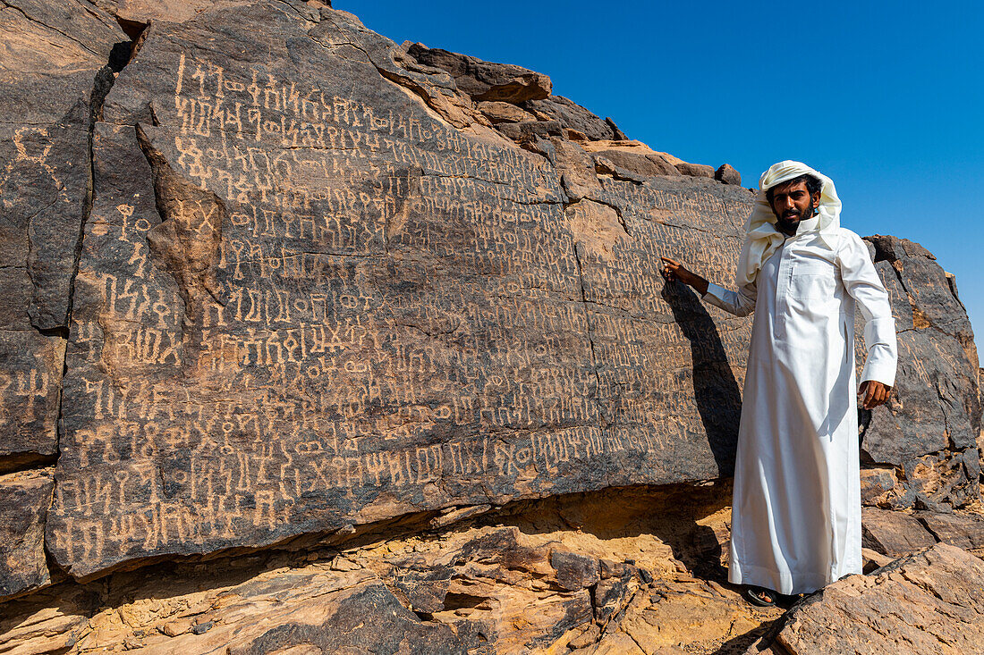 Man pointing at rock carvings, Bir Hima Rock Petroglyphs and Inscriptions, UNESCO World Heritage Site, Najran, Kingdom of Saudi Arabia, Middle East