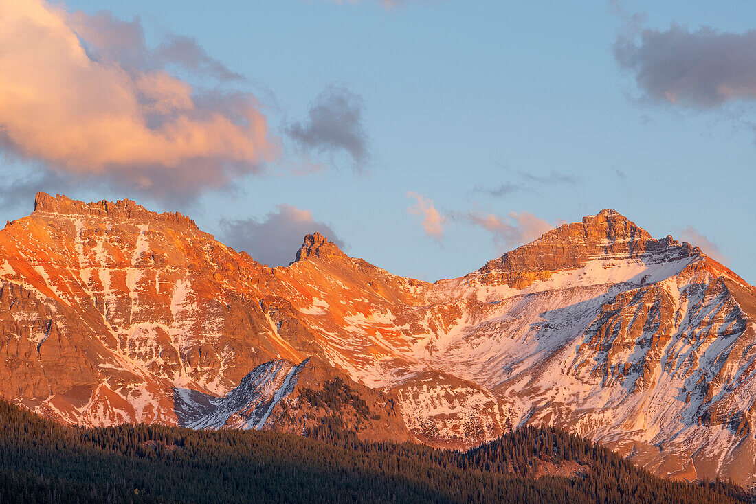 USA, Colorado. Uncompahgre National Forest, sunset light on Vermillion Peak above autumn evergreen forest, view east from above Trout Lake.