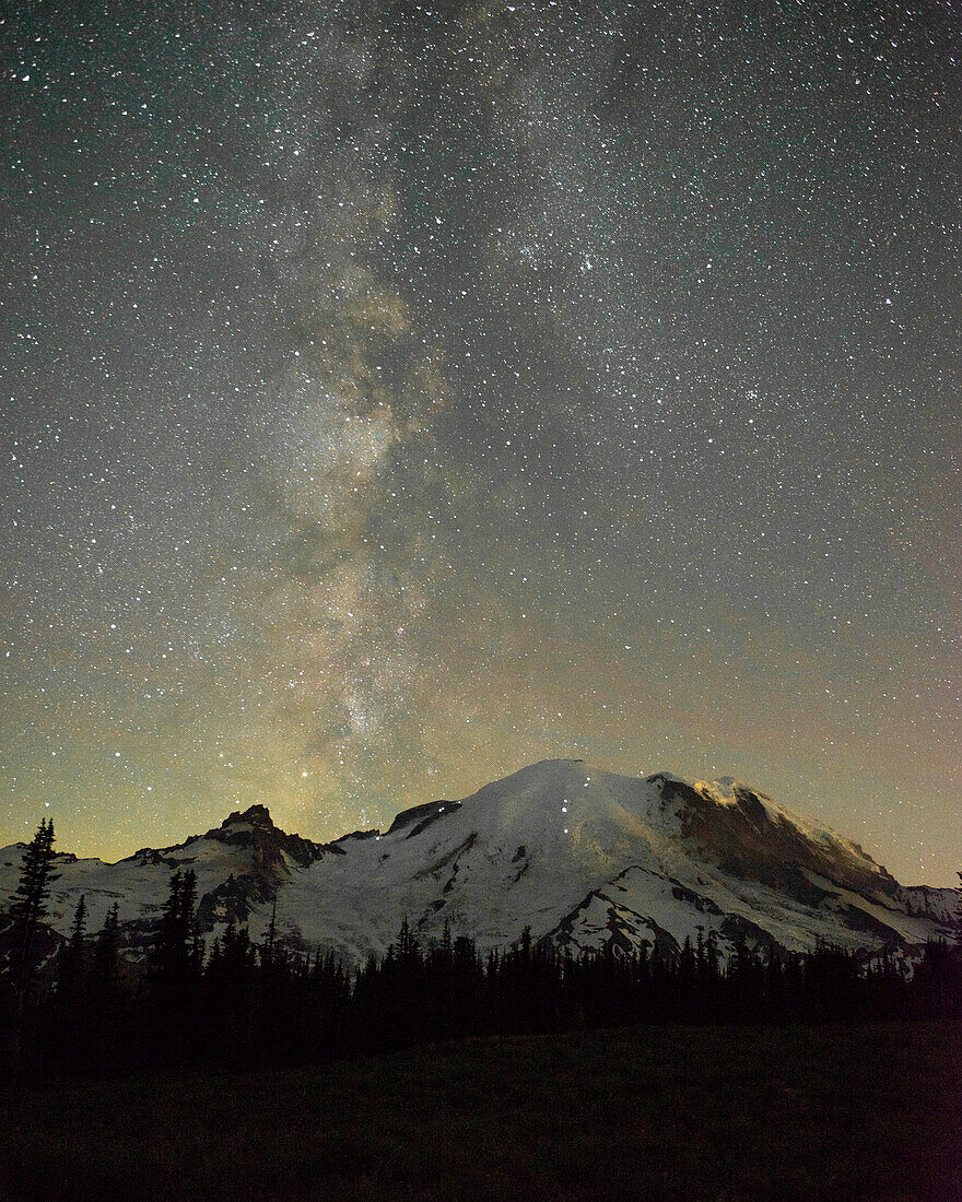 Die Lichter der Kletterer sind auf dem Berg zu sehen, wenn die Milchstraße hinter dem Mt. Rainier aufsteigt, Mt. Rainier-Nationalpark, US-Bundesstaat Washington.