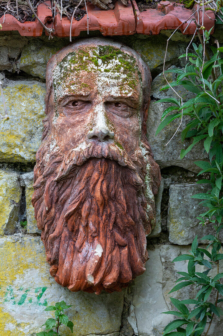 France, Giverny. Stone face hanging on a stone wall.