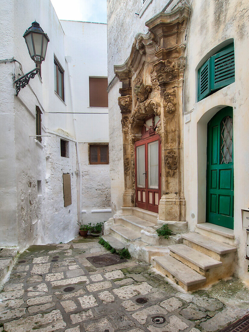 Italien, Apulien, Brindisi, Itria-Tal, Ostuni. Grüne Tür und eine rote Tür, umgeben von kunstvollen Schnitzereien in den Straßen und Gassen der Altstadt von Ostuni.