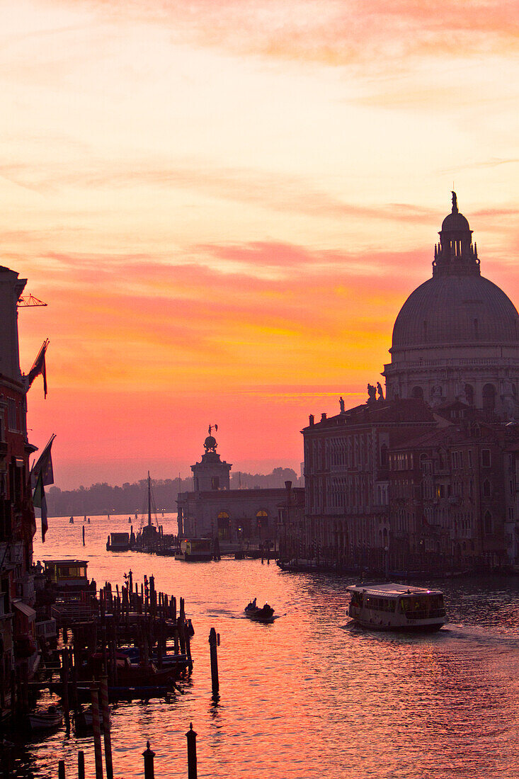 Venedig, Italien. Santa Maria della Salute, ein Wassertaxi, ein Motorboot und die Ponte dell'Accademia auf dem Canale Grande bei Sonnenaufgang