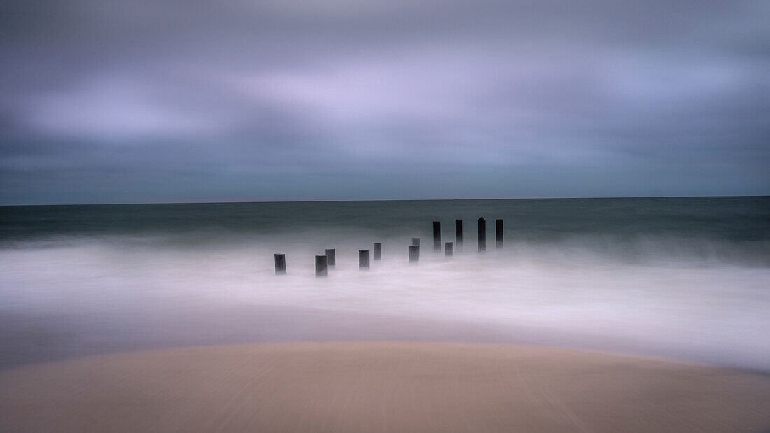 USA, New Jersey, Cape May National Seashore. Jetty supports and wave spry on beach.