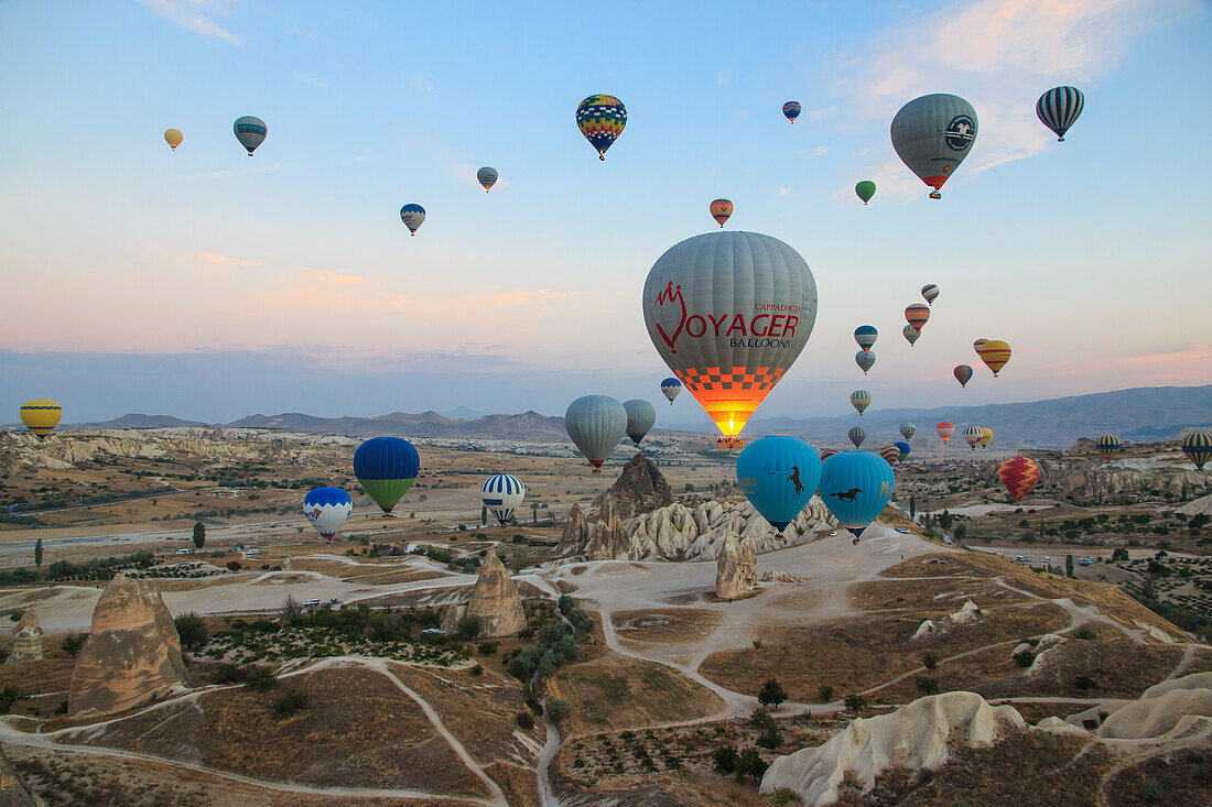 Turkey, Anatolia, Cappadocia, Goreme. Hot air balloons flying above rock formations and field landscapes in the Red Valley, Goreme National Park, UNESCO World Heritage Site.
