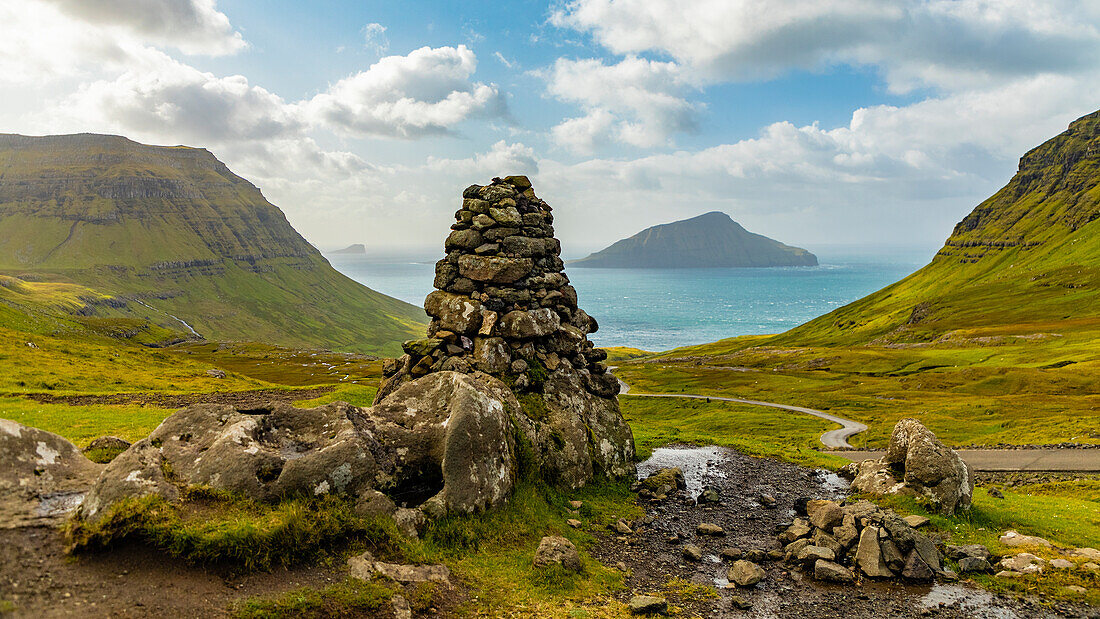 Europe, Faroe Islands. View of stone pillar overlooking the bay on the road to Nordradalur on the island of Streymoy