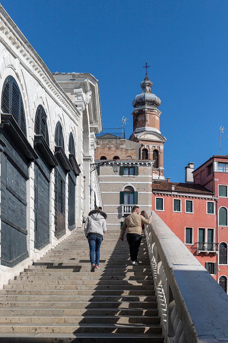 Two tourists climb the steps of the Rialto Bridge, Venice, Veneto, Italy