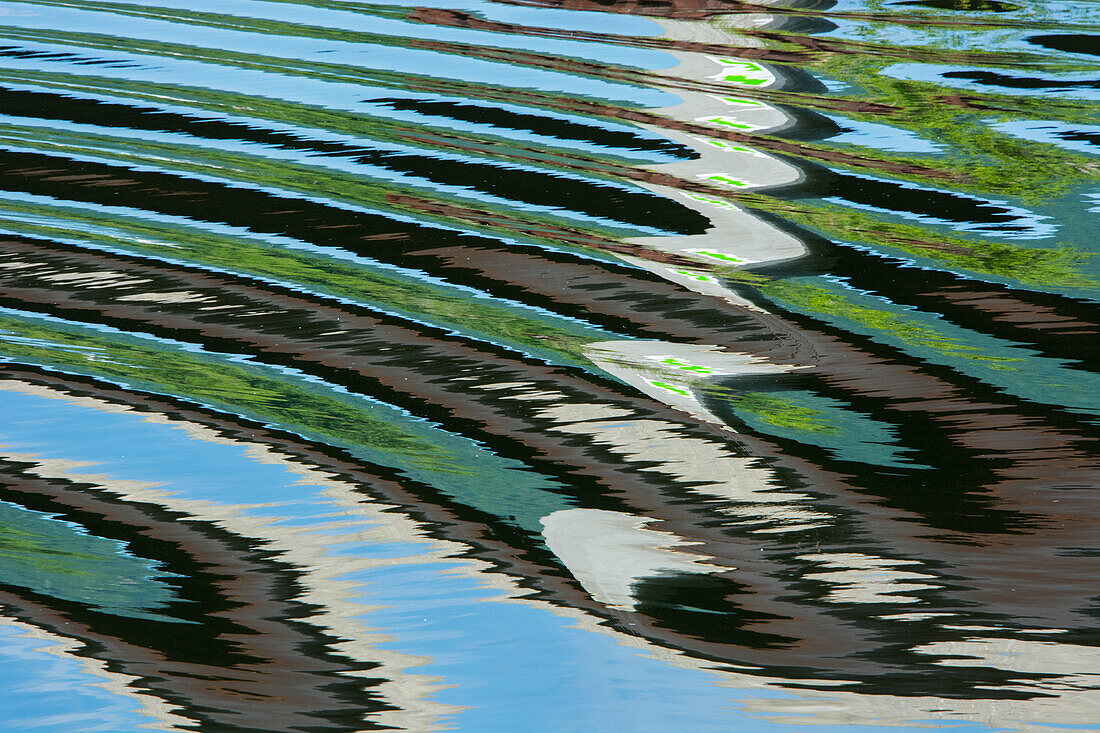 USA. Green trees reflected in river with ripples on the water.