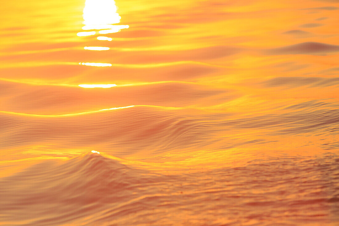 Sonnenuntergangsfarben und -muster auf kleinen Wellen im Wasser.