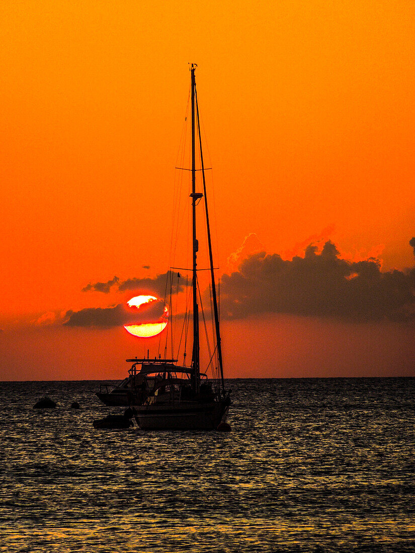 Seven Mile Beach, Grand Cayman. Segelboot und ein Boot mit orangefarbenem Sonnenuntergang hinter den Wolken am Karibischen Meer