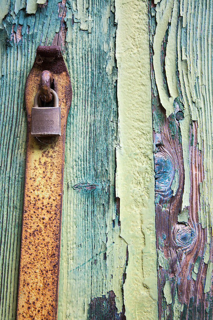 Italien, Venedig, Insel Burano. Muster von abblätternder Farbe und Vorhängeschloss an alten Holztüren.