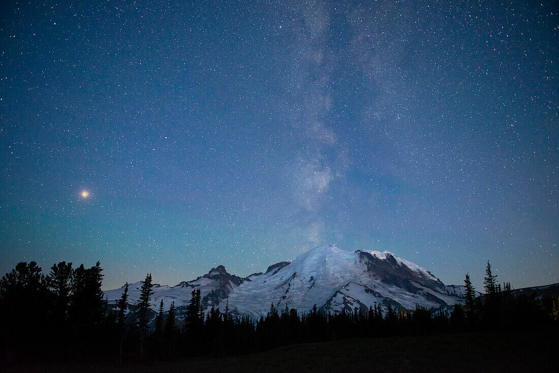 The lights of climbers can be seen on the mountain as the Milky Way rises behind Mt. Rainier National Park, Washington State.