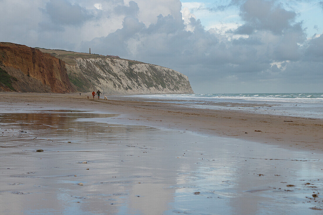 Couple with a dog strolling along the beach at Yaverland Beach on the Isle of Wight with chalk cliffs in the background